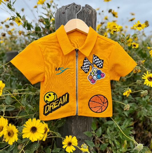 Yellow children's jacket with patches on a wooden post surrounded by yellow flowers.